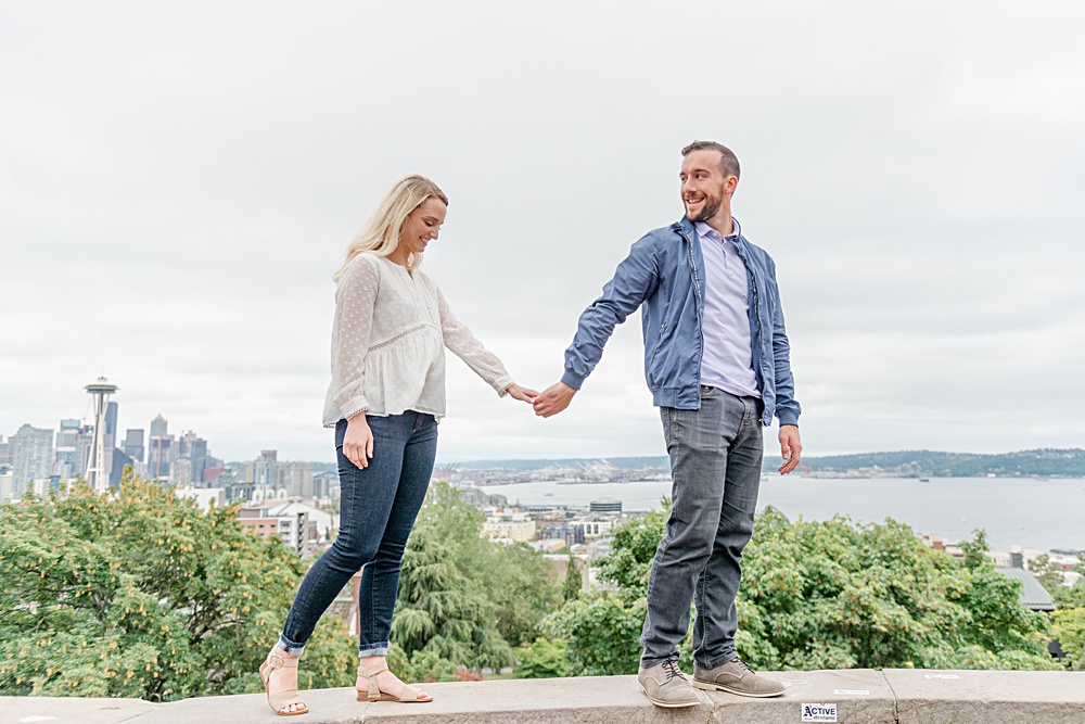 Couple walks along ledge with the Seattle skyline behind them