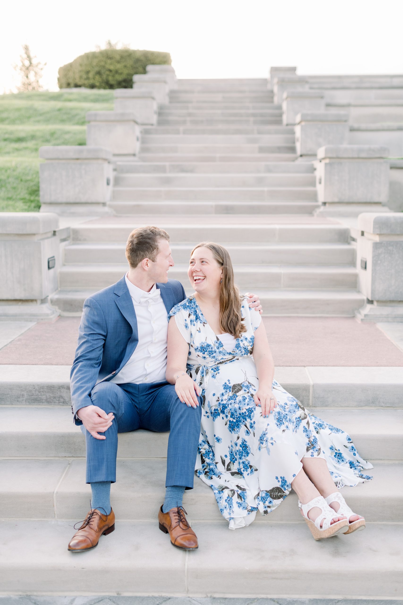 Couple share a smile on the steps during engagement session at Coxhall Gardens in Carmel, Indiana