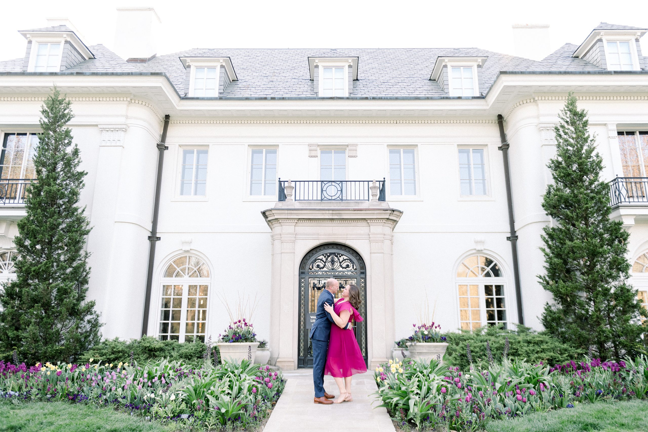 Couple stand in front of Lilly House during spring engagement session at Newfields