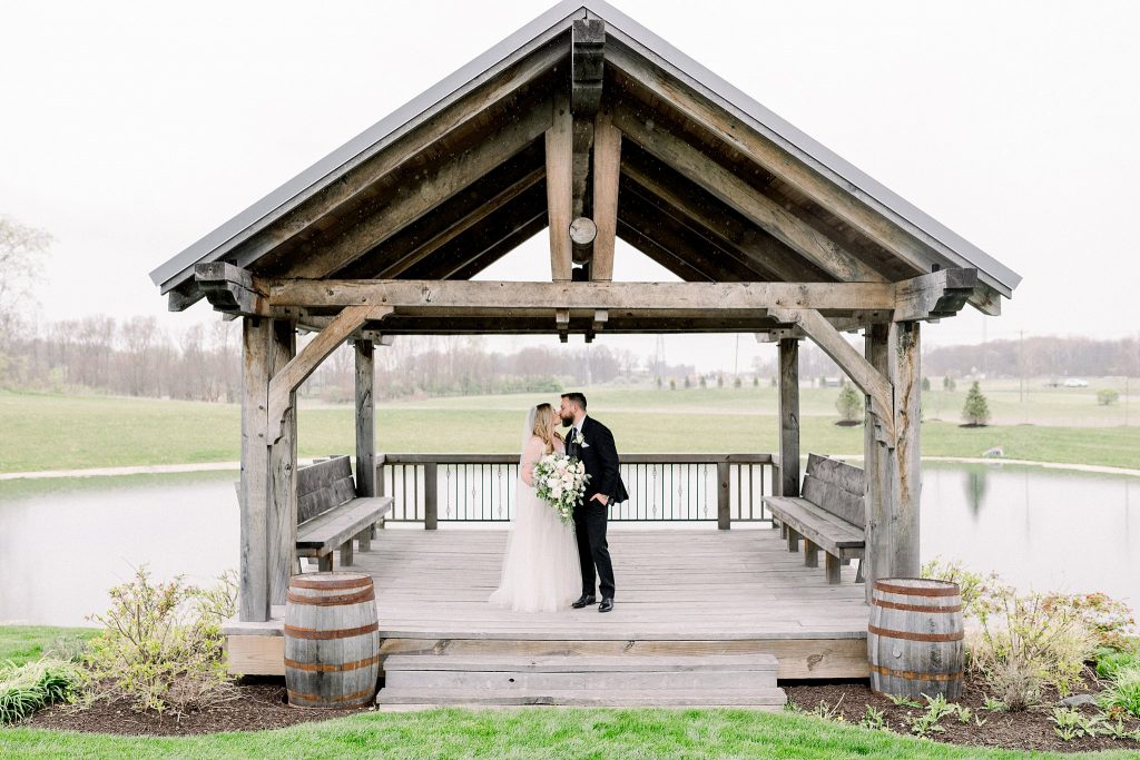 Bride and groom share a kiss under covering during rain shower on their wedding day at Lindley Farmstead