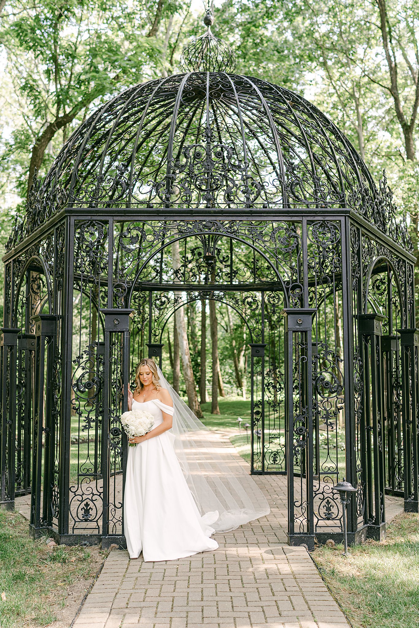 Bride standing against a black iron gazebo with her veil blowing gently in the wind at Black Iris Estate